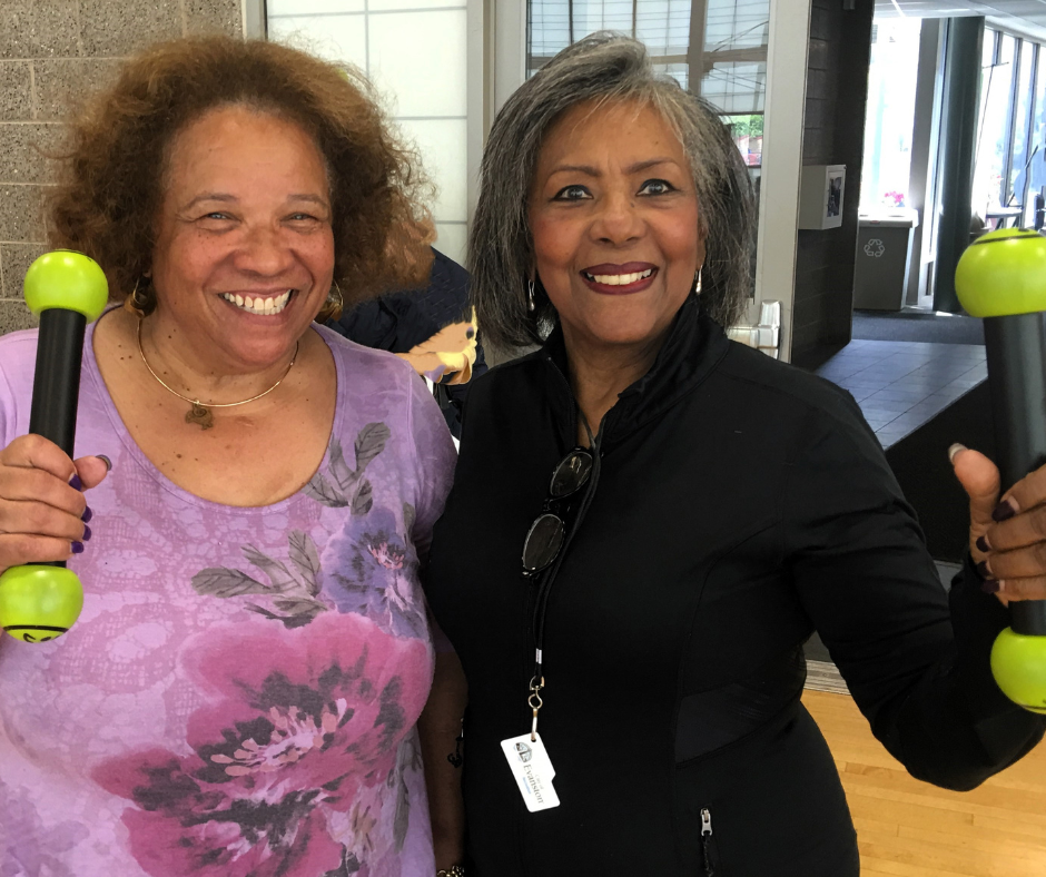 two ladies who are smiling and holding hand weights